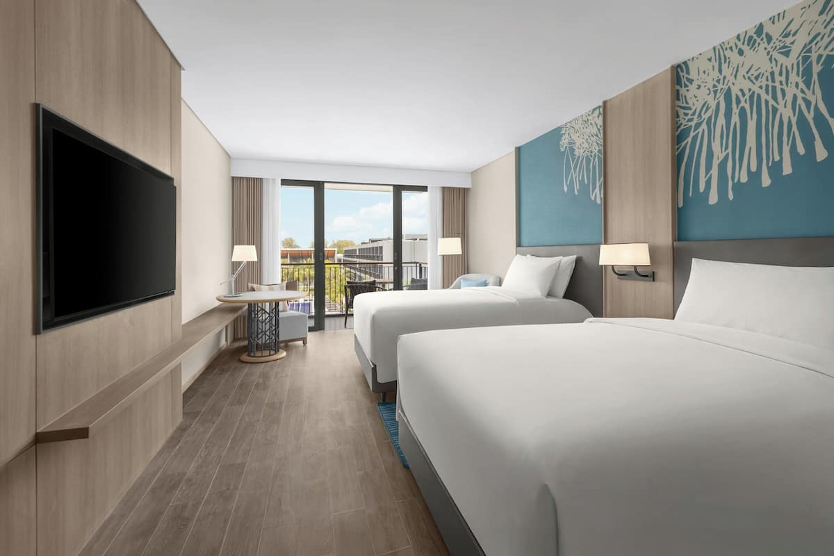 Een hotelkamer met twee bedden, een televisie, een balkon met uitzicht en een schilderij aan de muur.