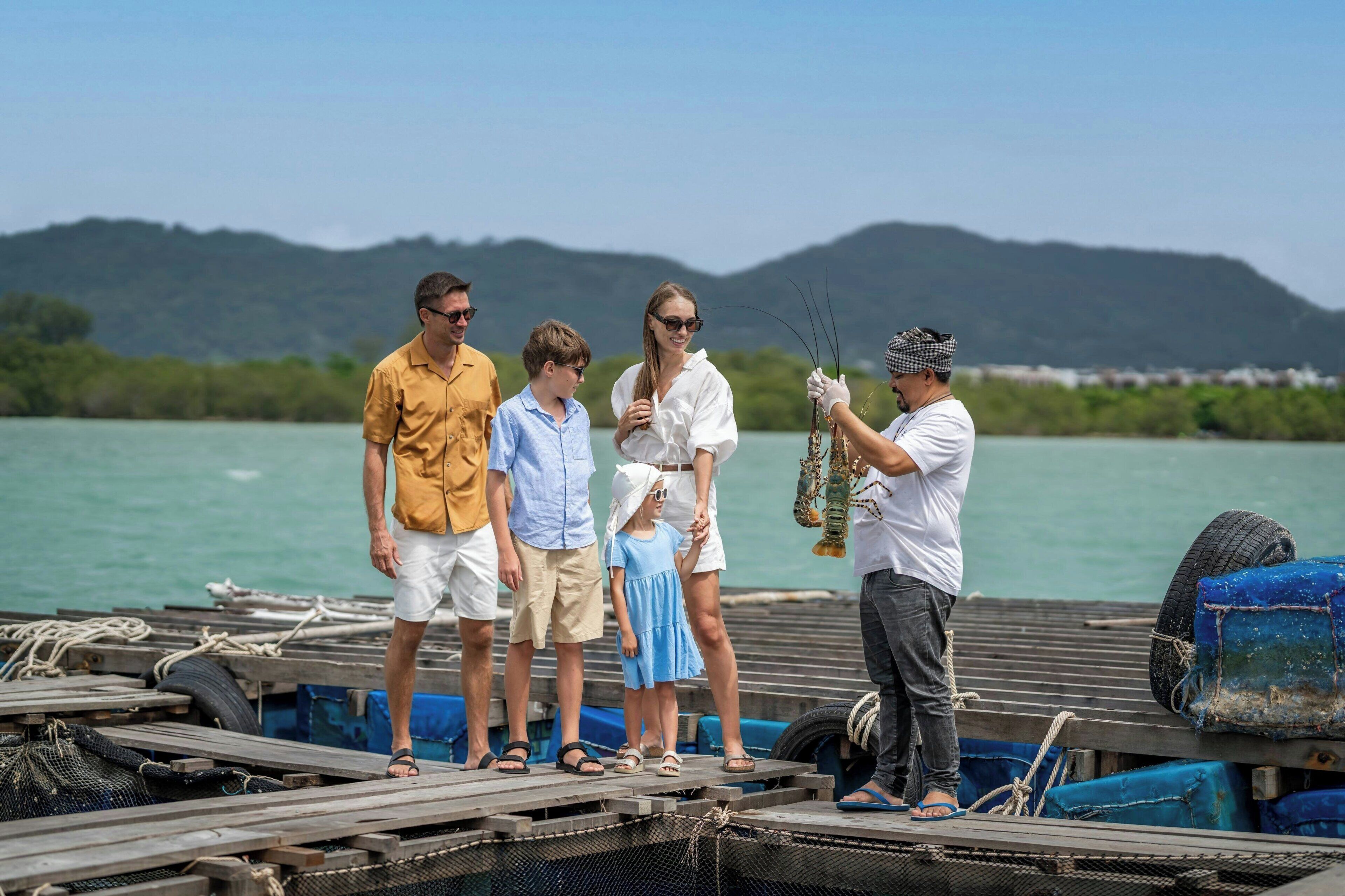 Un grupo de personas en un muelle, con una masa de agua y colinas al fondo.