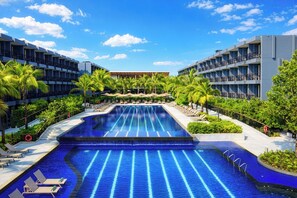 Une piscine dotée de plusieurs couloirs, entourée de palmiers et de chaises longues, avec un bâtiment en arrière-plan.