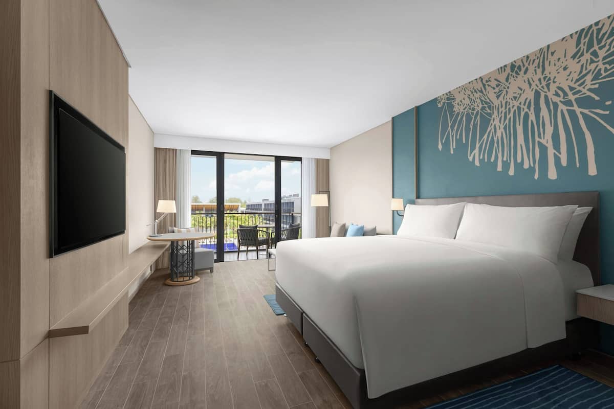 Een moderne hotelkamer met een groot bed, een flatscreen-tv, een balkon met een tafel en stoelen, en uitzicht op de stad.