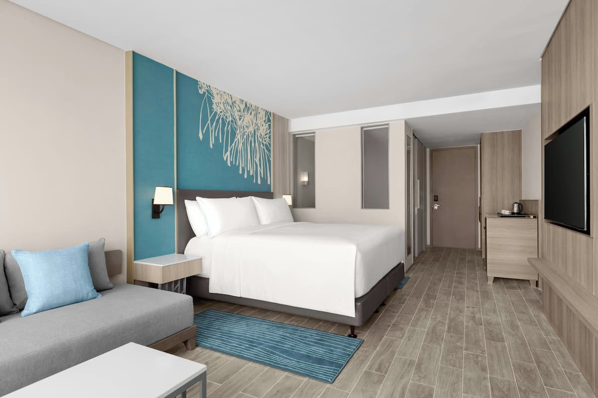 Een hotelkamer met een bed, een bank, een televisie, een bureau en een schilderij aan de muur.