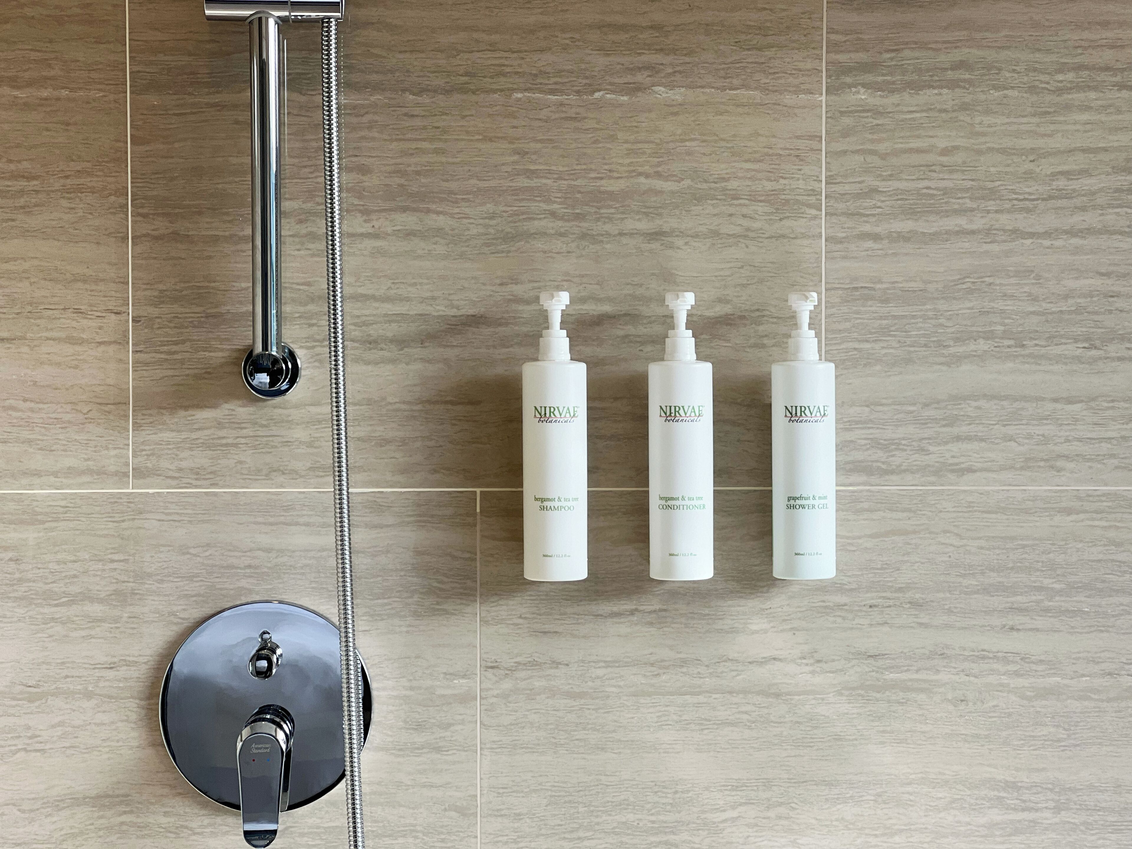 Une salle de bain équipée d’une douche, d’un pommeau de douche à main et de trois flacons de produits de la marque Nirvae Botanicals.