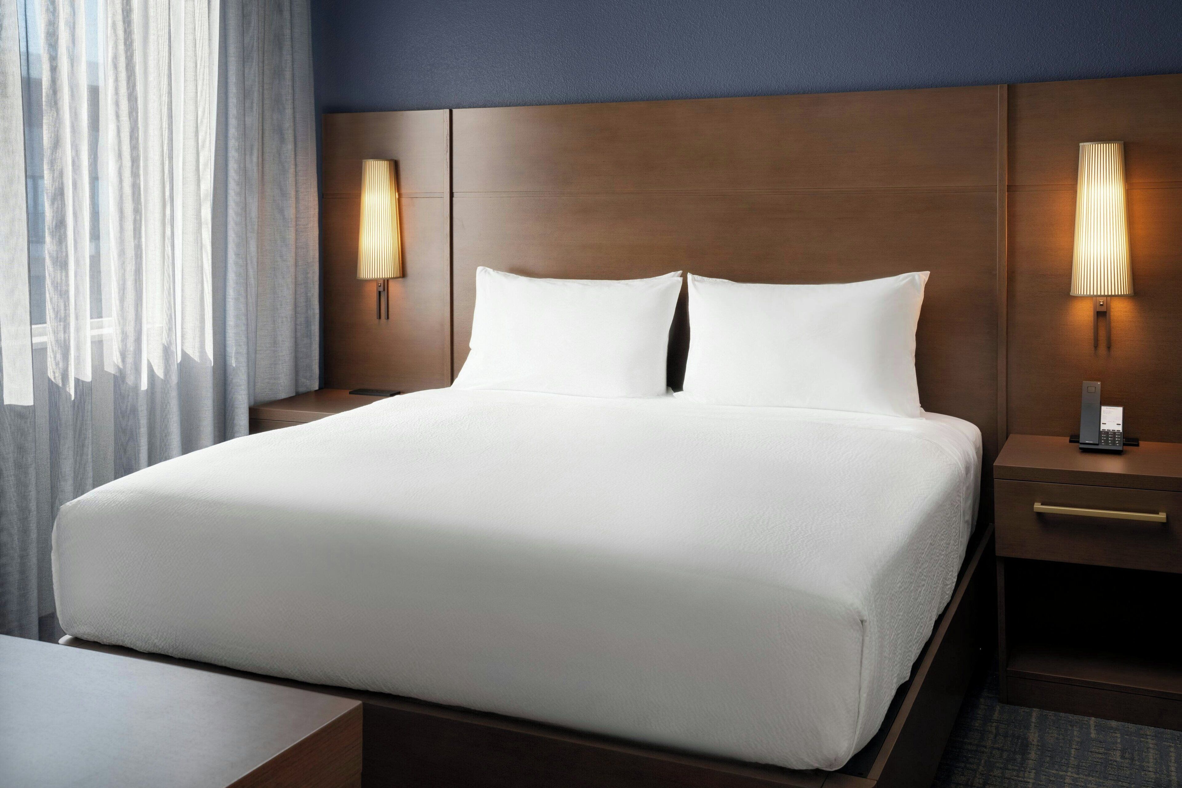 A hotel room with a large bed, two bedside tables with lamps, and a window with curtains.