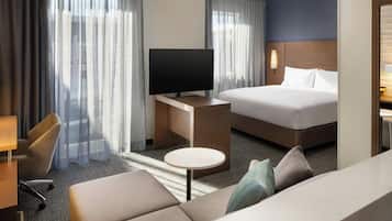 Camera d'albergo con un letto, una TV su un mobile in legno, un divano, un tavolino rotondo e una sedia.