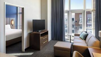 A hotel room with a bed, a TV on a wooden stand, a sofa, and a small table.