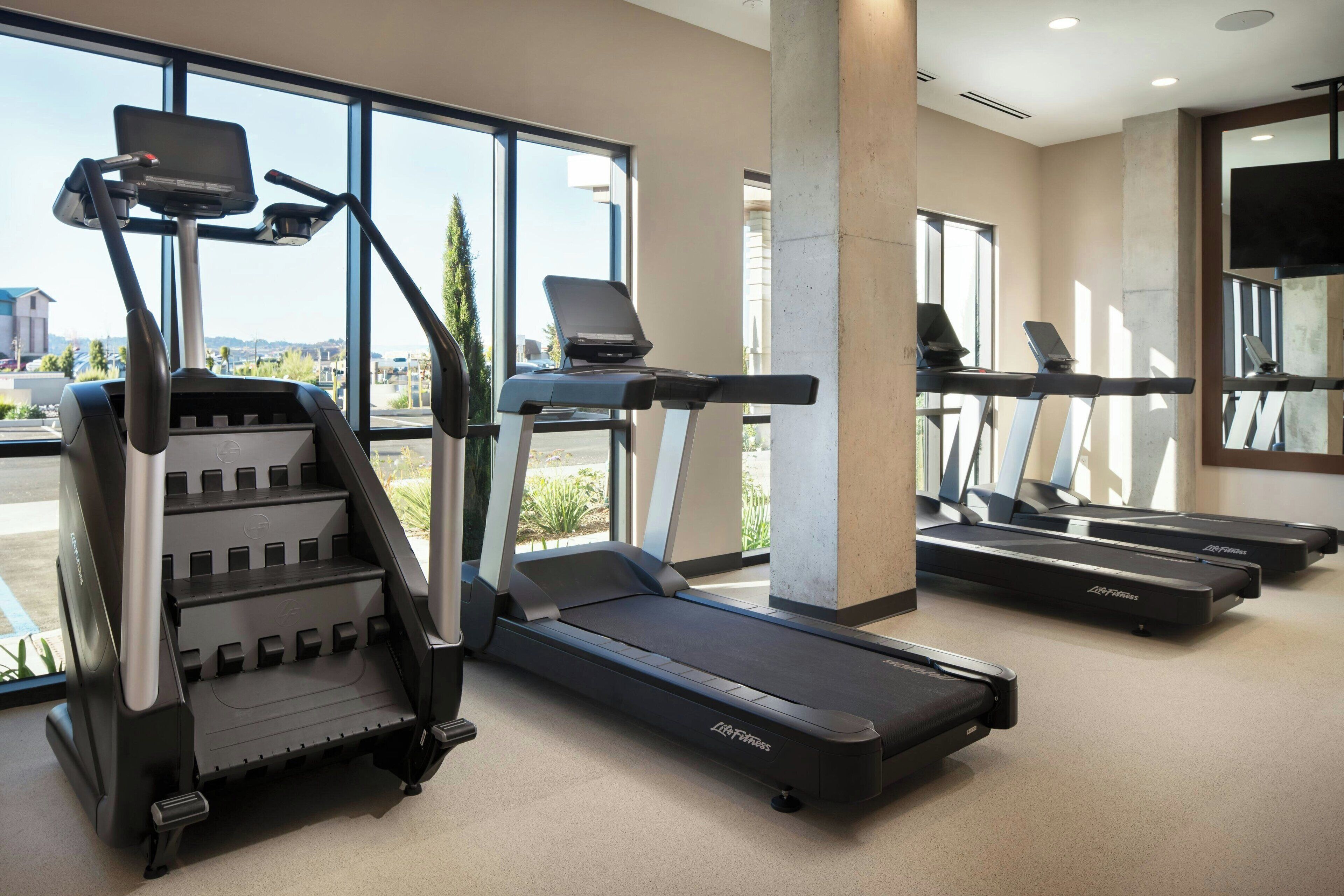Une salle de sport équipée de tapis de course, d’un appareil d’escalier et d’un tapis de course avec un support pour ordinateur portable.