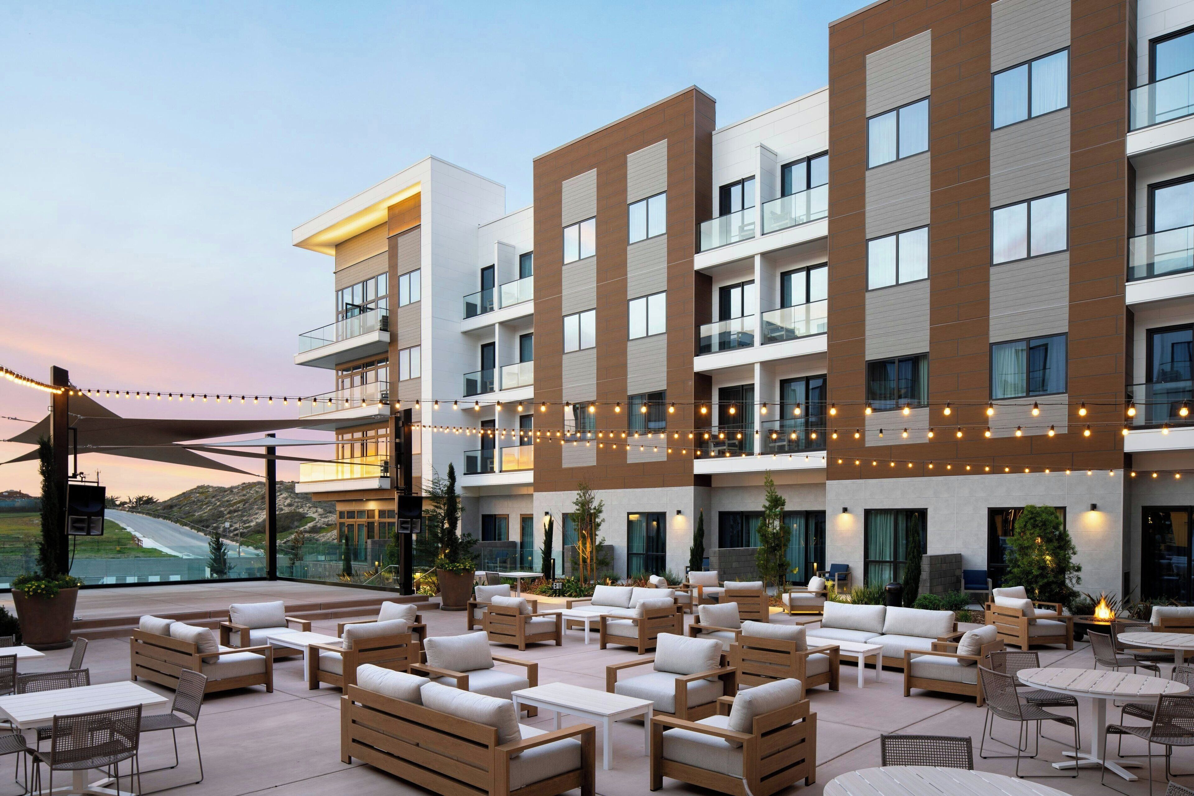 Un hotel moderno con asientos al aire libre, varios balcones y vistas al paisaje.