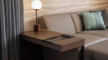 Een moderne hotelkamer met een houten bureau, een lamp, een afstandsbediening en een bank met een groen kussen.