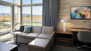 Et moderne hotelværelse med et stort vindue, der giver udsigt over et smukt landskab, en sofa, et skrivebord med lampe og en stol.