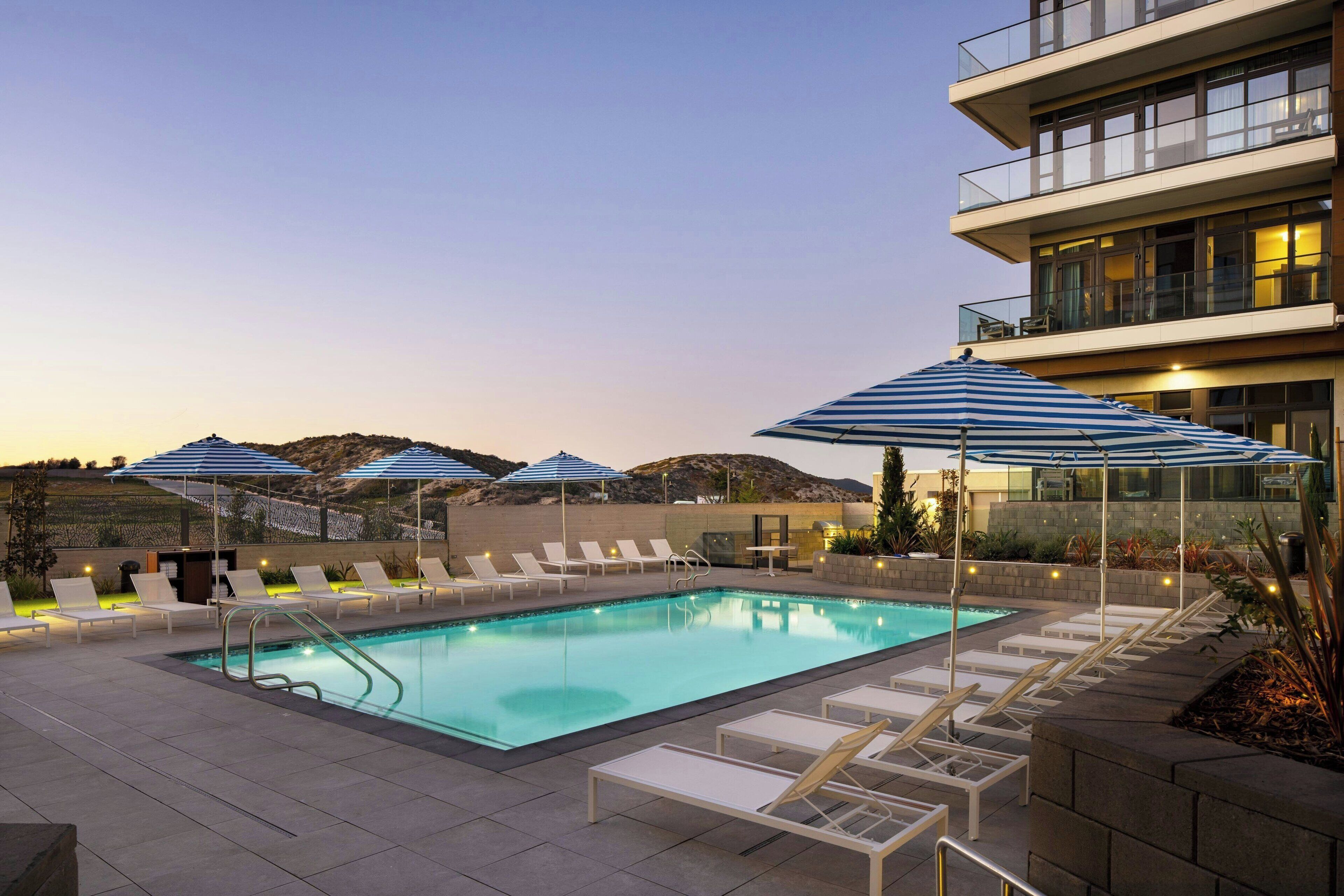 A pool area with lounge chairs and umbrellas, surrounded by a modern building with a pool view.
