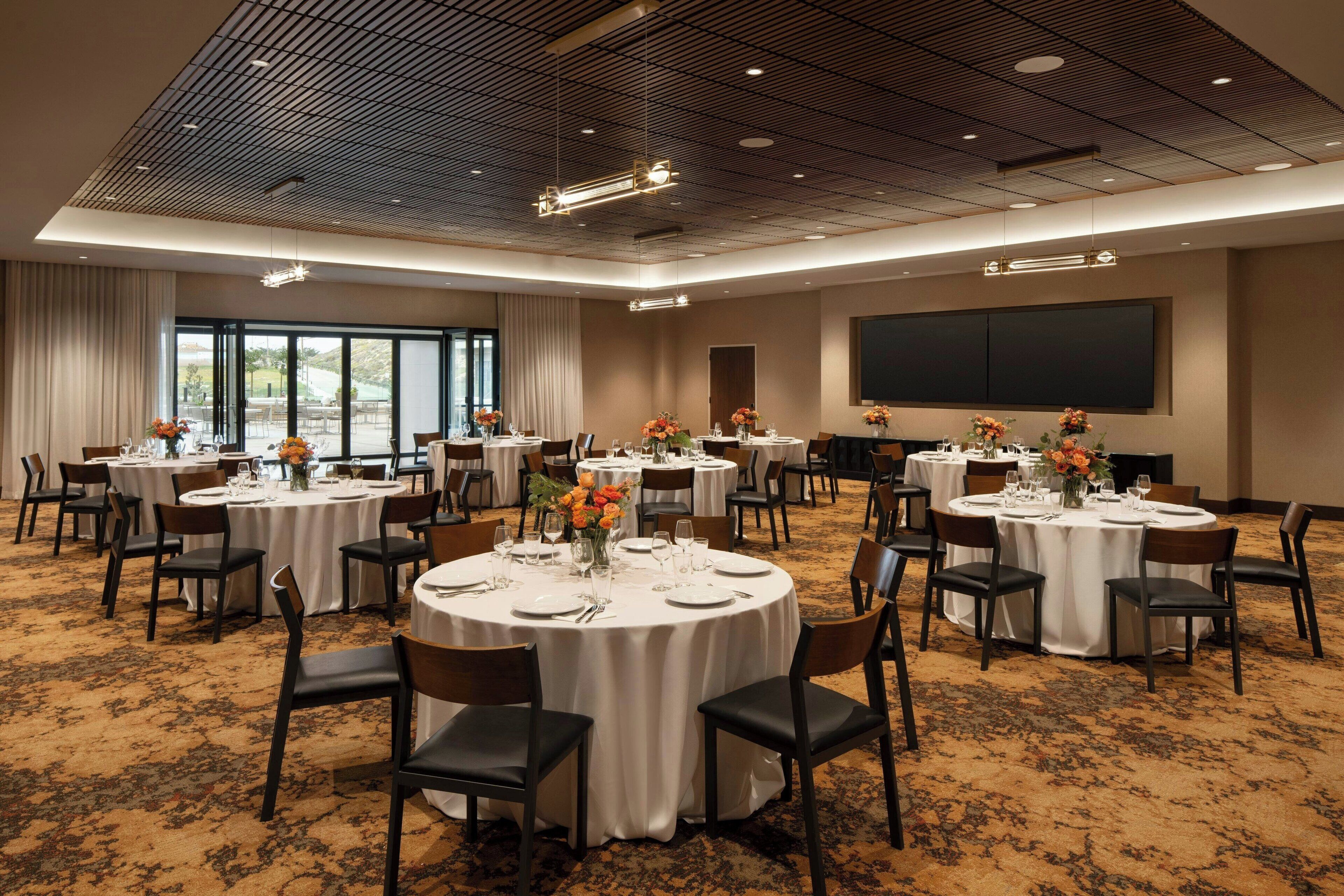 A conference room with multiple round tables, each set with chairs, white tablecloths, and flower centerpieces.