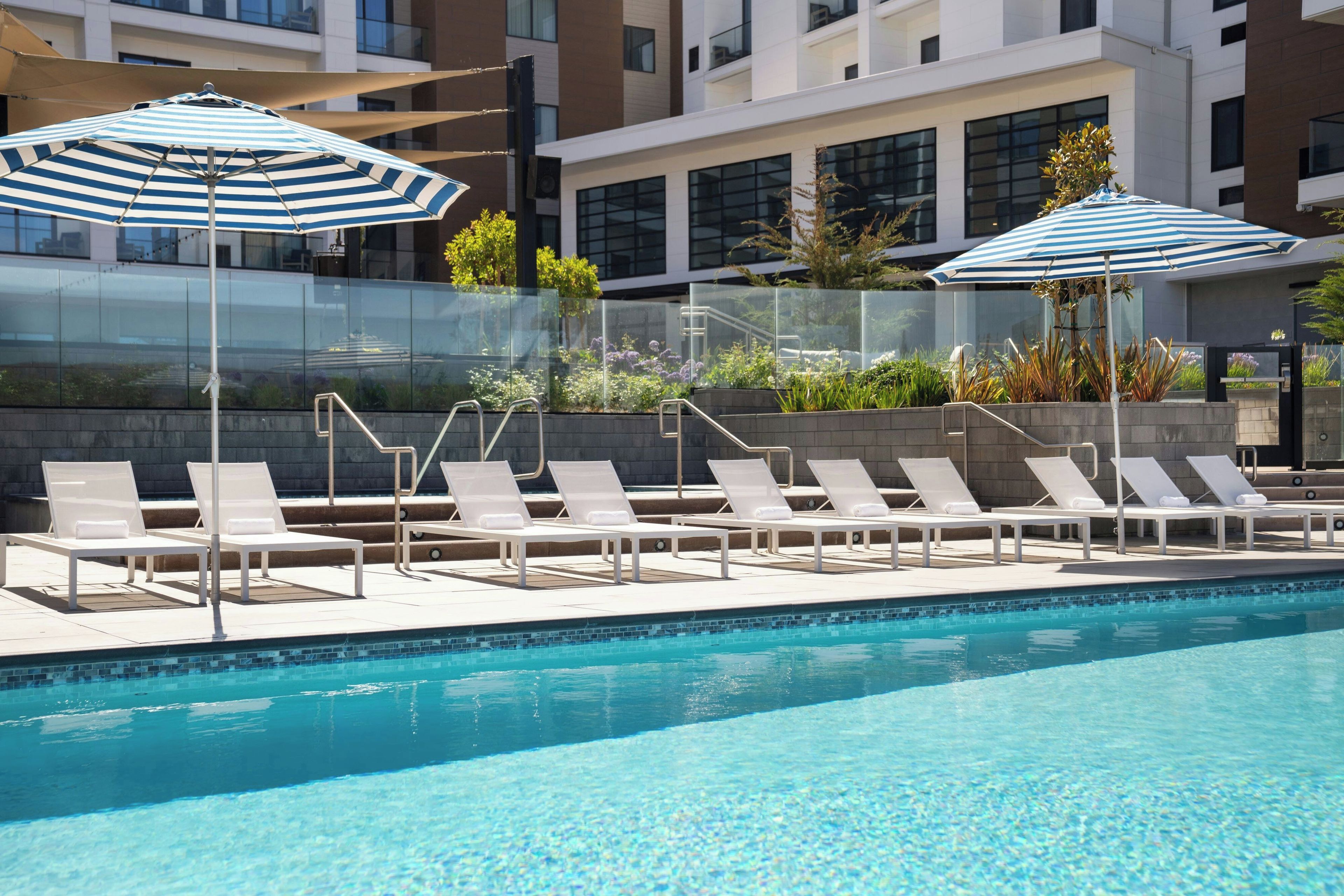 A poolside area with lounge chairs and umbrellas, surrounded by a modern building with glass walls.