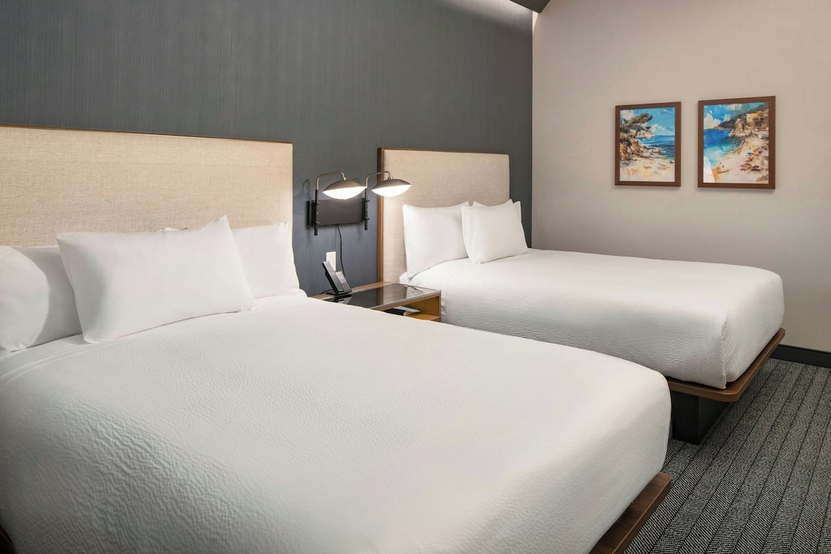 A hotel room with two beds, a nightstand with a lamp, and two framed pictures on the wall.