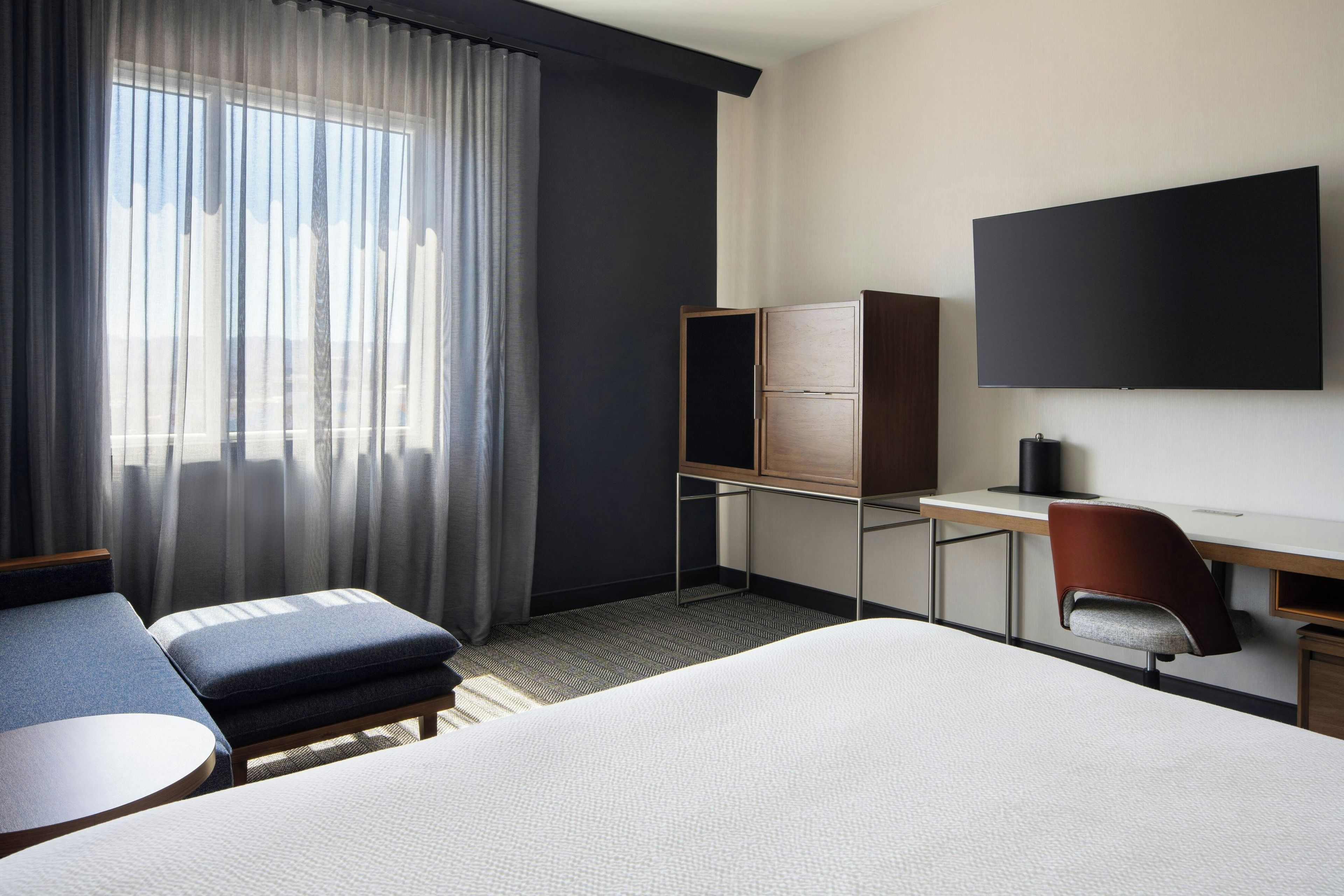 Een hotelkamer met een bed, bureau, stoel, televisie en een raam met gordijnen.