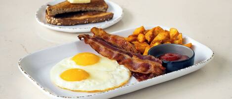 A breakfast plate with eggs, bacon, hash browns, toast, and ketchup.