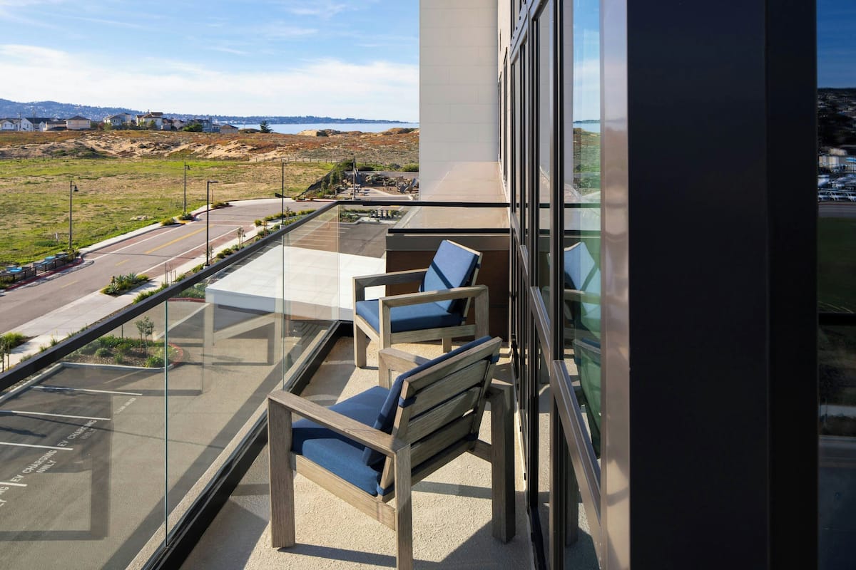 Un balcon avec deux chaises en bois et une balustrade en verre donnant sur une route et un paysage lointain.