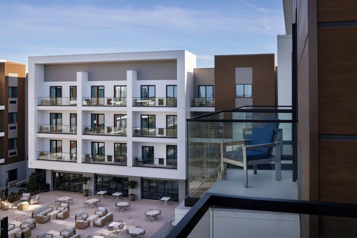Un hôtel à plusieurs étages doté d’espaces extérieurs aménagés pour s’asseoir, de balcons et de grandes fenêtres.