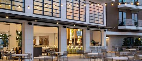 An outdoor dining area with tables and chairs, a bar, and a view of the building's interior.