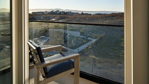 A balcony with a wooden chair, a glass railing, and a view of a hilly landscape with buildings in the distance. - Courtyard By Marriott Sand City Monterey (Seaside)