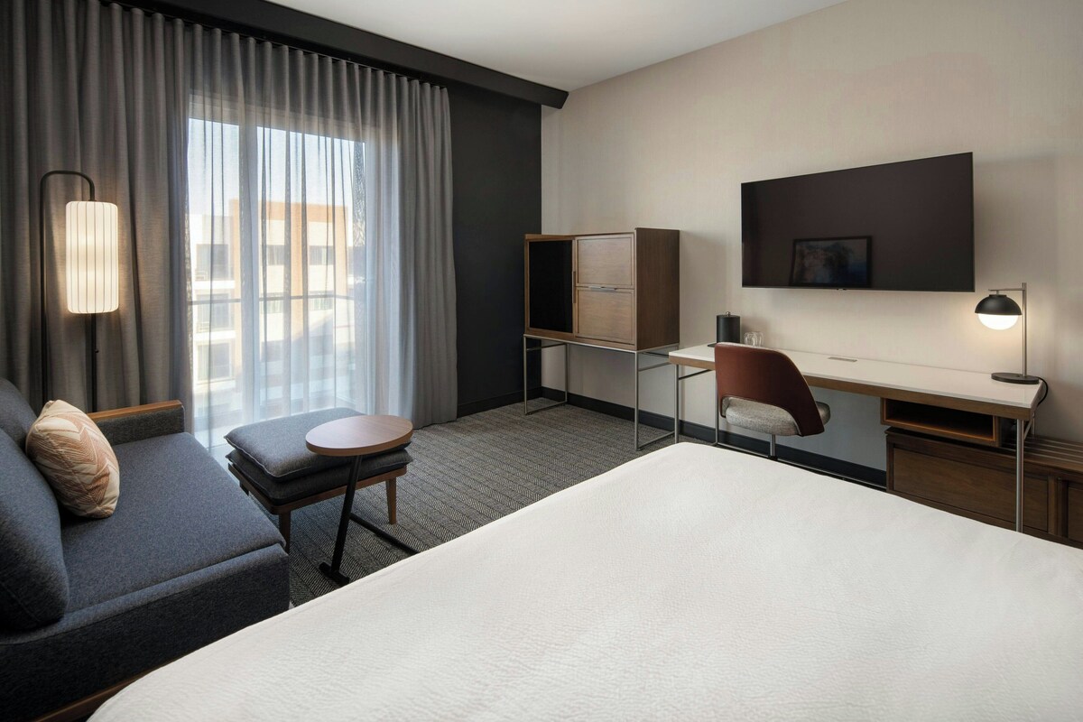 Habitación de hotel con una cama grande, un escritorio, una silla, un sofá y un televisor en la pared.