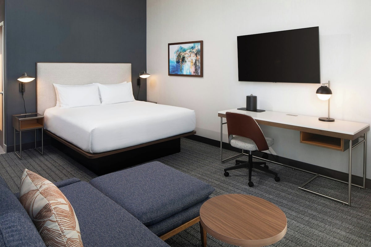 Une chambre d’hôtel équipée d’un lit, d’un bureau, d’une chaise, d’un canapé et d’une télévision.