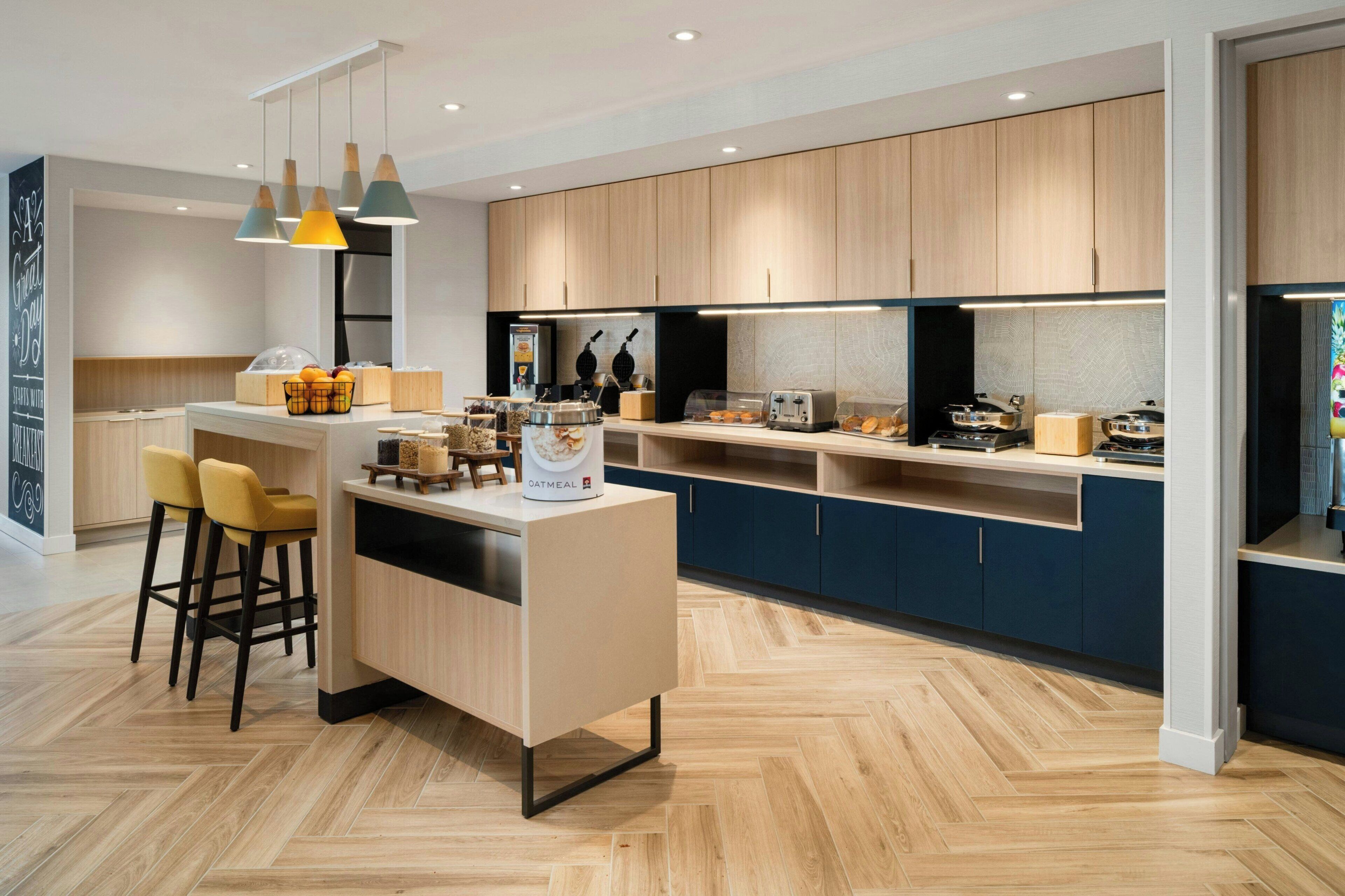 A modern kitchen with wooden cabinets, a central island, bar stools, and pendant lighting.