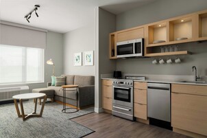 Una cocina moderna con electrodomésticos integrados, una zona de comedor con sofá y mesa, y un ventanal que proporciona luz natural.