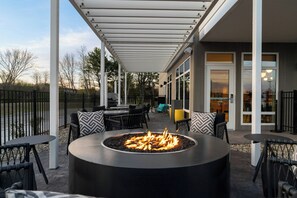 Een terras buiten met een rond vuurkorf, zitplaatsen buiten en een overdekt gedeelte met uitzicht op het interieur.