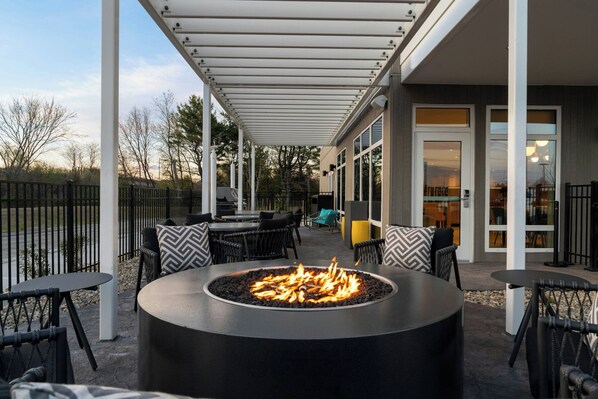 An outdoor patio with a circular fire feature, outdoor seating, and a covered area with a view of the interior. - Towneplace Suites By Marriott Seekonk (Seekonk)