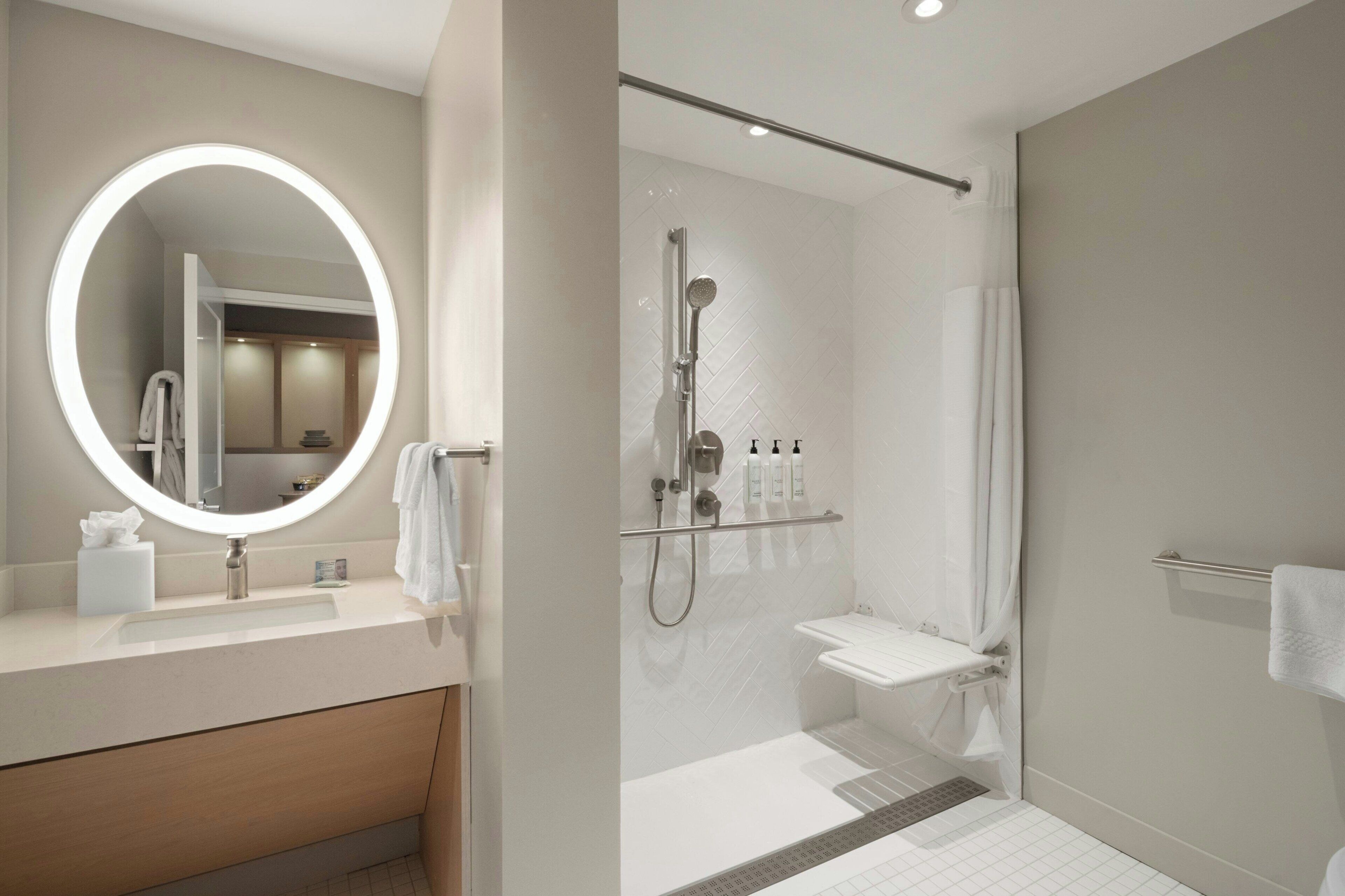A modern bathroom with a round mirror, a shower, and a vanity with a sink.
