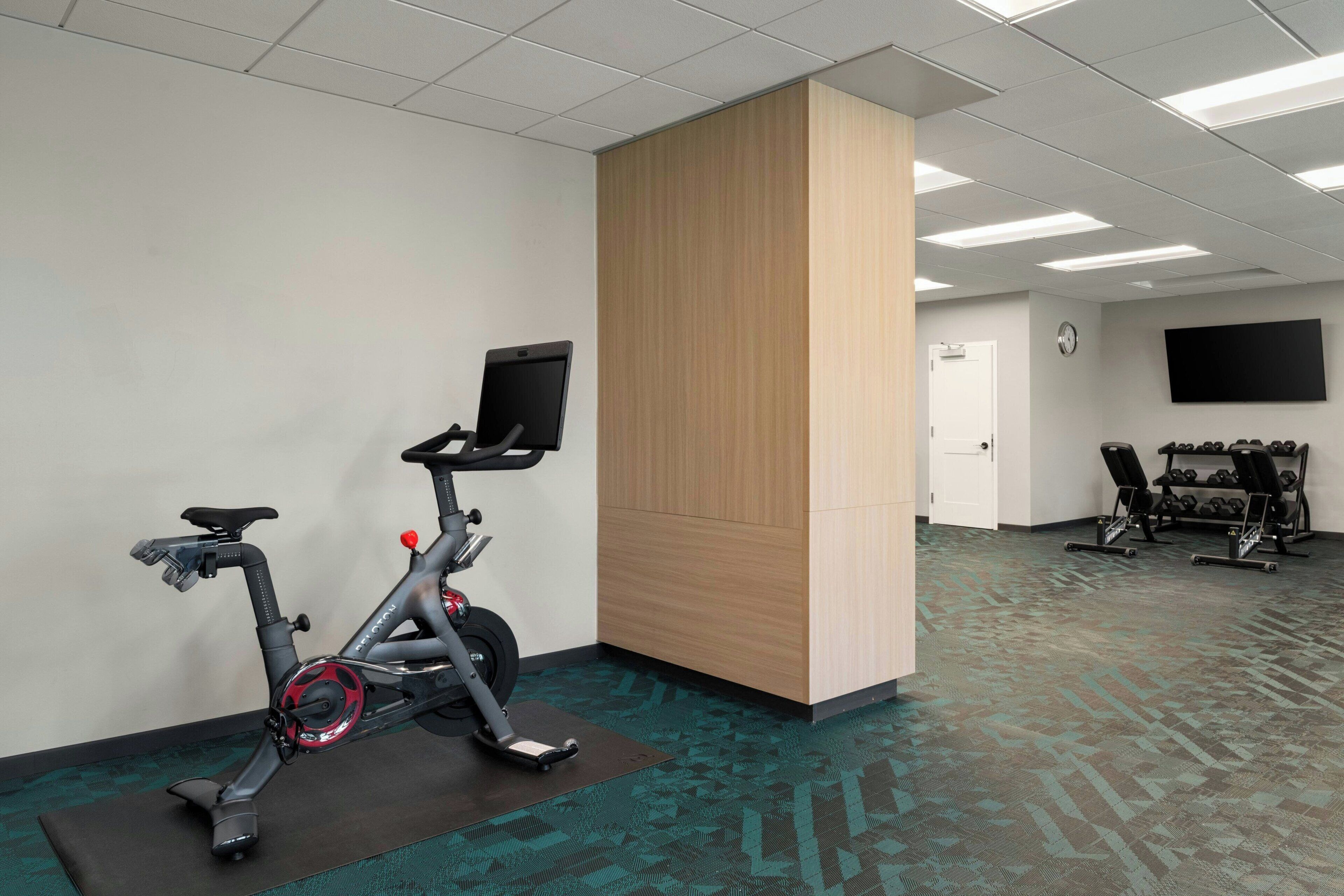 A fitness room with exercise bikes, a television, and a wall-mounted clock.