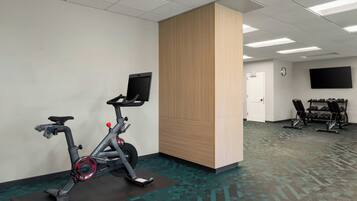 Une salle de remise en forme équipée de vélos d’exercice, d’un téléviseur et d’une horloge murale.