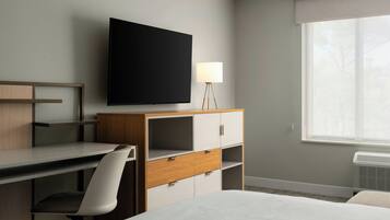 A hotel room with a bed, a desk, a chair, a television, a lamp, and a window.
