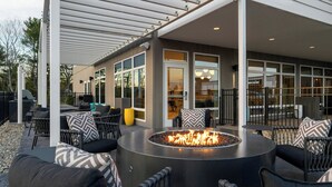 Un espacio al aire libre con una chimenea circular, mobiliario de mimbre y un porche cubierto.