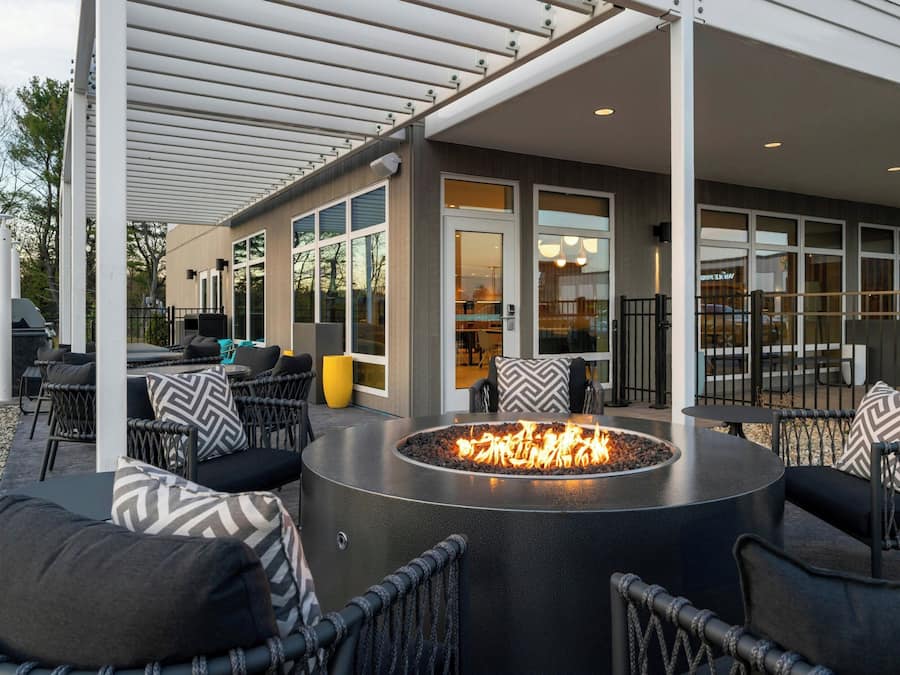Un espacio al aire libre con una chimenea circular, mobiliario de mimbre y un porche cubierto.