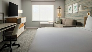 Habitación de hotel con cama, escritorio, silla, televisor, sofá, lámpara y ventana.