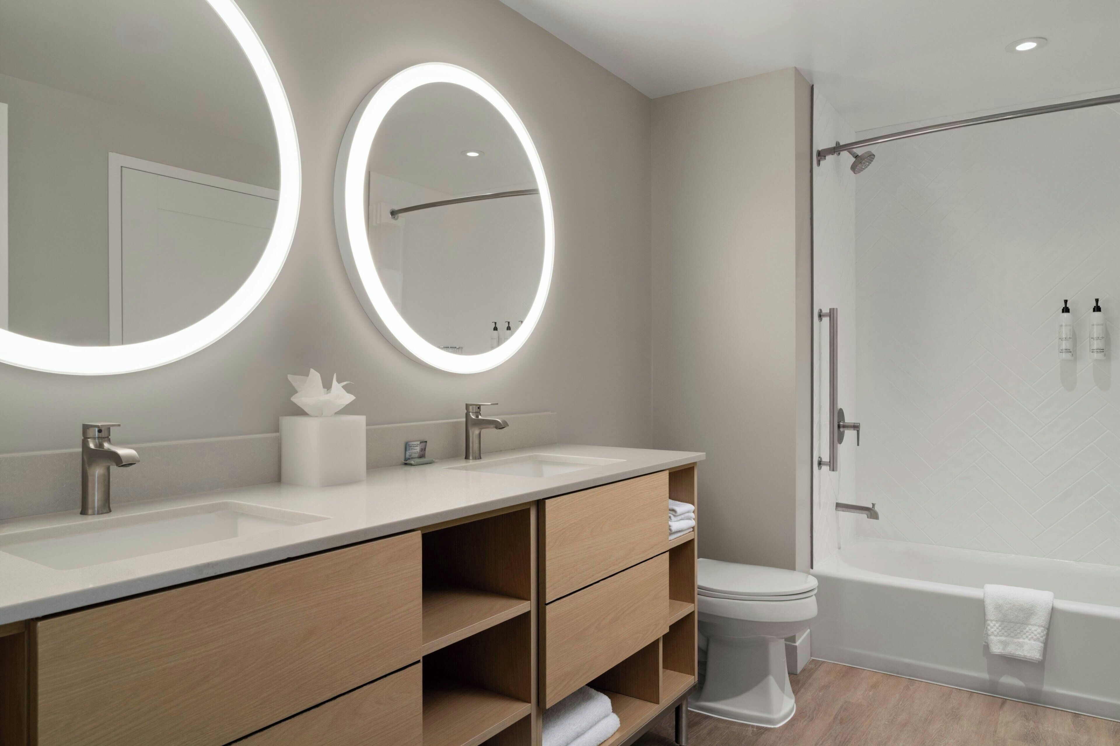 A modern bathroom with two round mirrors, a vanity with a sink, a toilet, and a shower area.