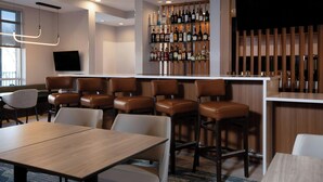 A modern bar area with wooden bar stools, a television mounted on the wall, and a variety of liquor bottles on shelves. - Springhill Suites By Marriott Richmond Airport (Sandston)