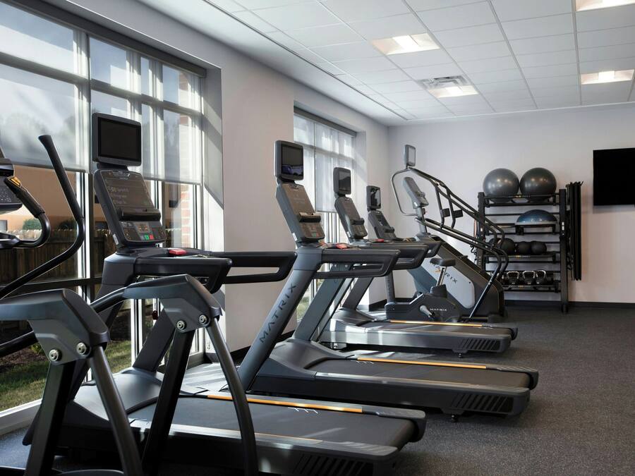 Academia com esteiras, bolas de exercício e uma tela de televisão.