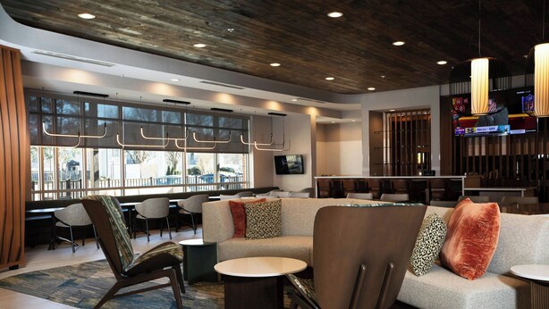 A modern lobby with a sofa, chairs, a round table, and a TV screen. - Springhill Suites By Marriott Richmond Airport (Sandston)