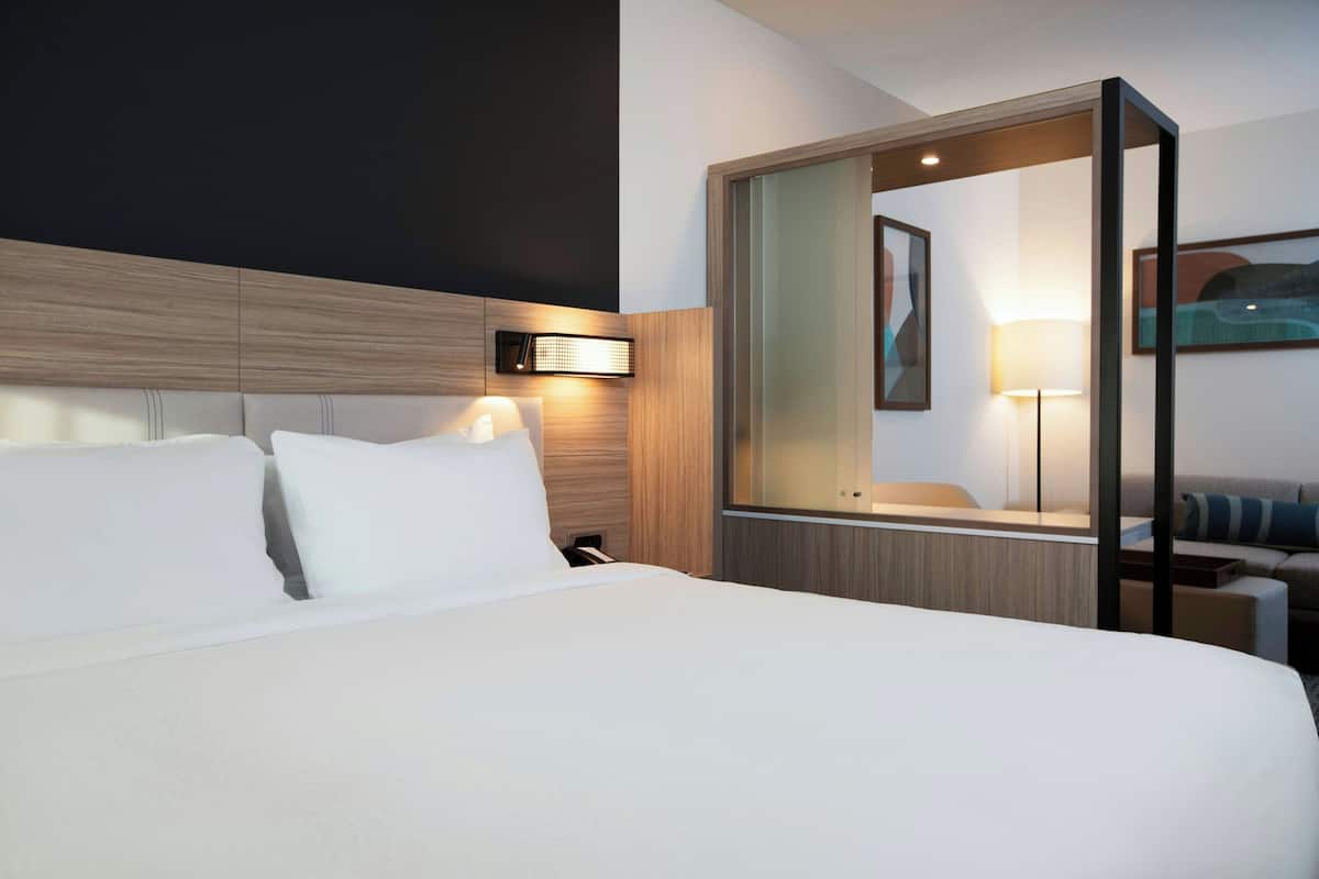 A hotel room with a large bed, a bedside table, a mirror, and a wall-mounted light fixture.