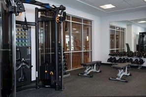 Un gimnasio con equipo de levantamiento de pesas, bancos y mancuernas.