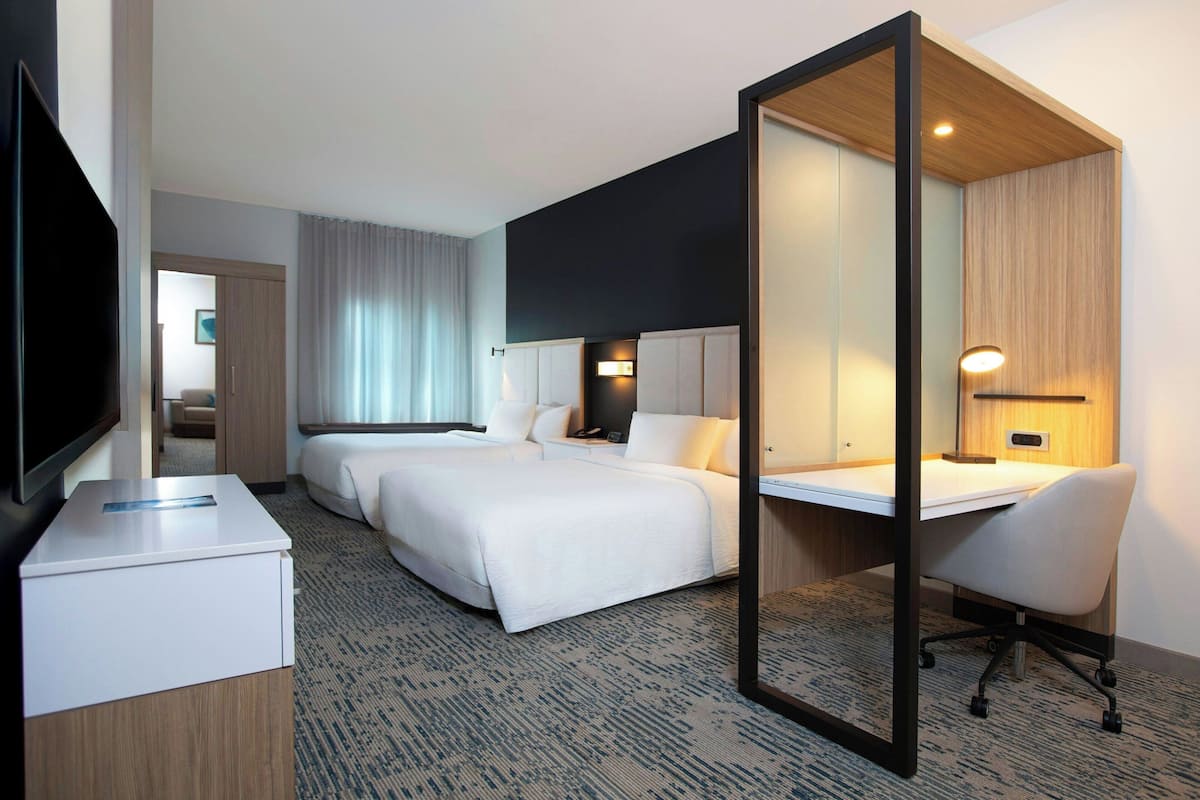 A hotel room with two beds, a desk, a chair, a TV, and a mirror.