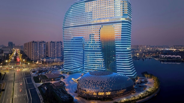 Un hotel moderno con una estructura en forma de cúpula distintiva, un amplio frente de cristal y ubicación frente al agua.