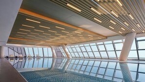 Una piscina interior moderna con un diseño geométrico en el techo y ventanas amplias.