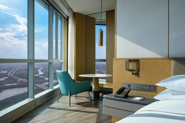 Une chambre d’hôtel avec une grande fenêtre, un lit, un bureau avec un téléphone, une chaise et une table.