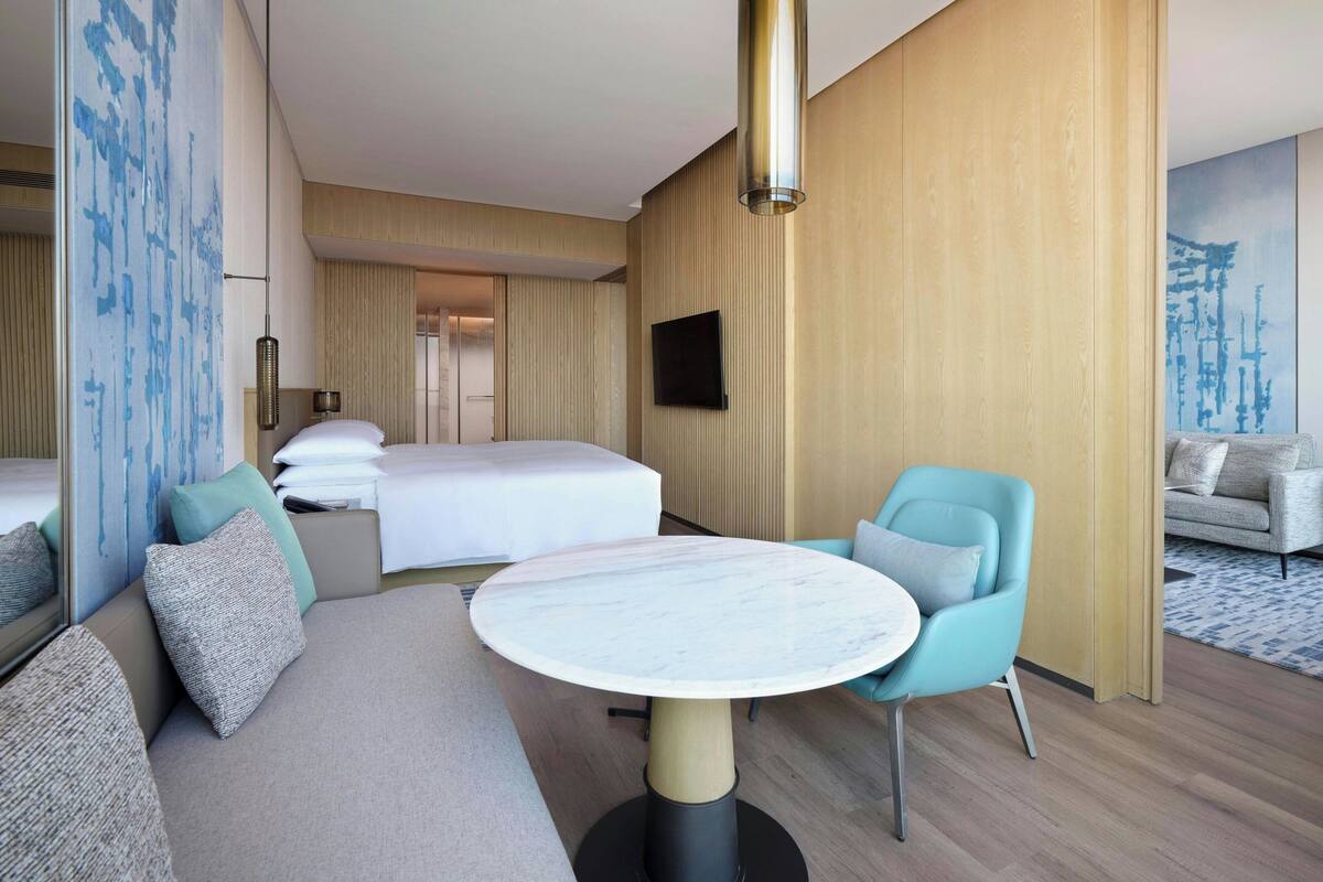 A hotel room with a bed, a sofa, a round table, and a TV mounted on the wall.