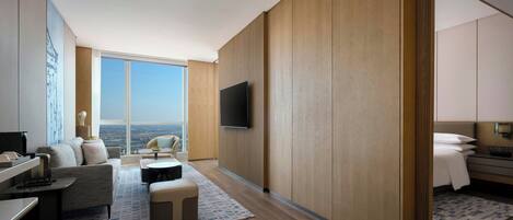 A modern hotel room with a large window, a flat-screen TV, a sofa, a coffee table, and a bed.