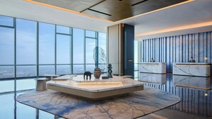 Un moderno vestíbulo de hotel con una fuente de mármol en el centro, amplias ventanas con vistas a la ciudad y un mostrador de recepción.