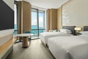 Een hotelkamer met twee bedden, een bureau, een stoel, een televisie en een groot raam met uitzicht.